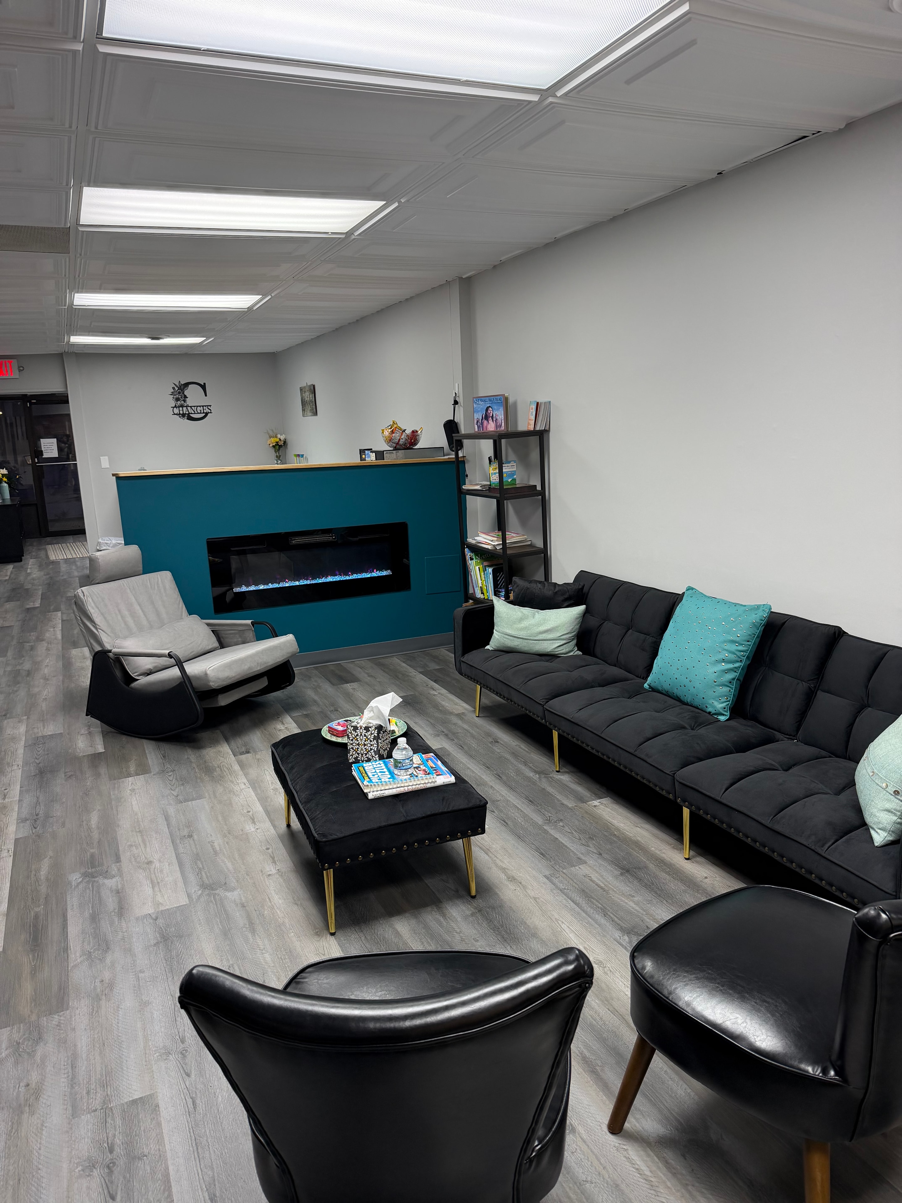 Changes Therapeutic Services waiting area with teal fireplace accent wall, black sofa with teal pillows, and Changes logo sign