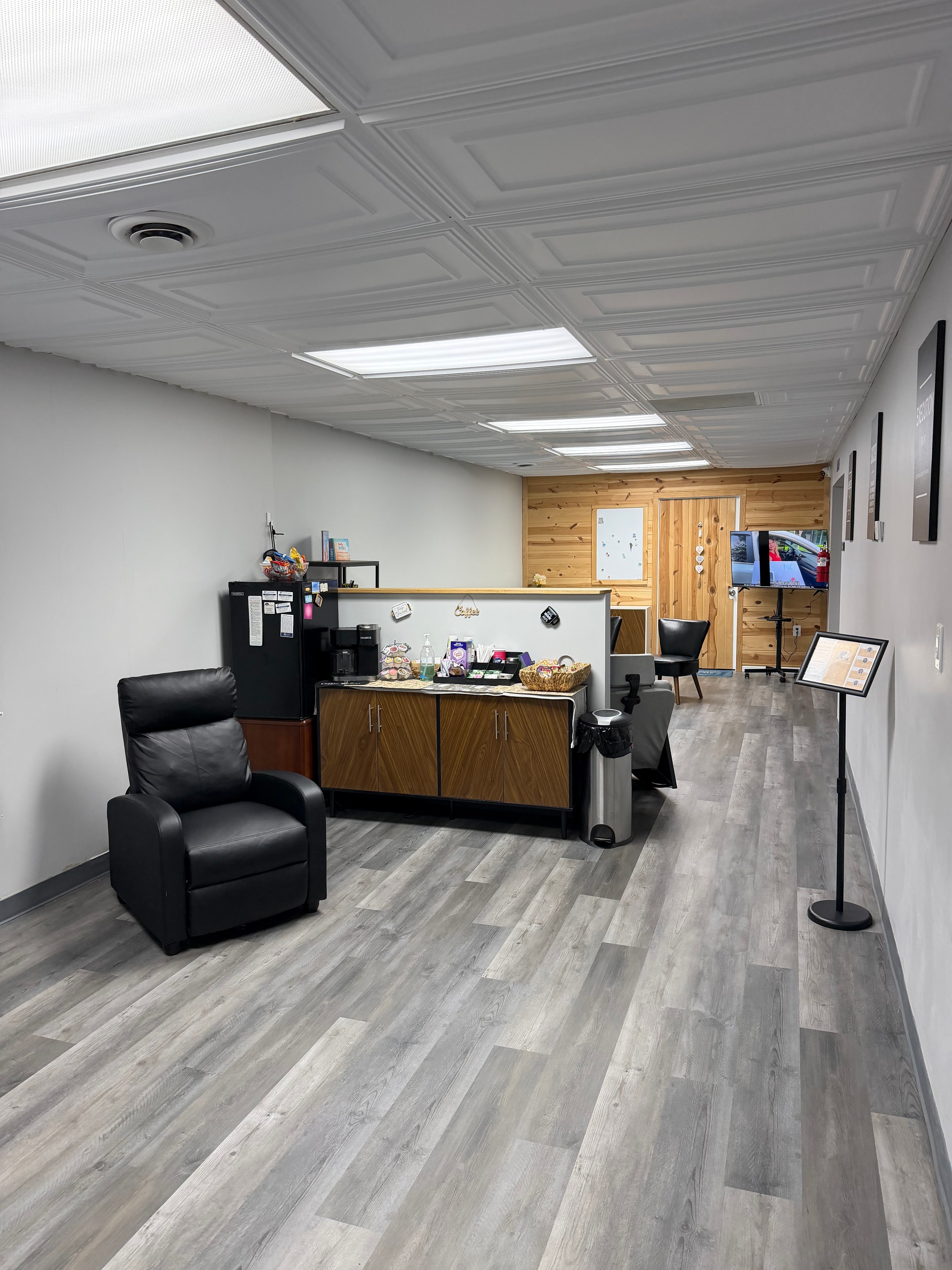 Changes Therapeutic Services lounge area with coffee station, black recliner, wood accent wall, and hallway leading to therapy suites