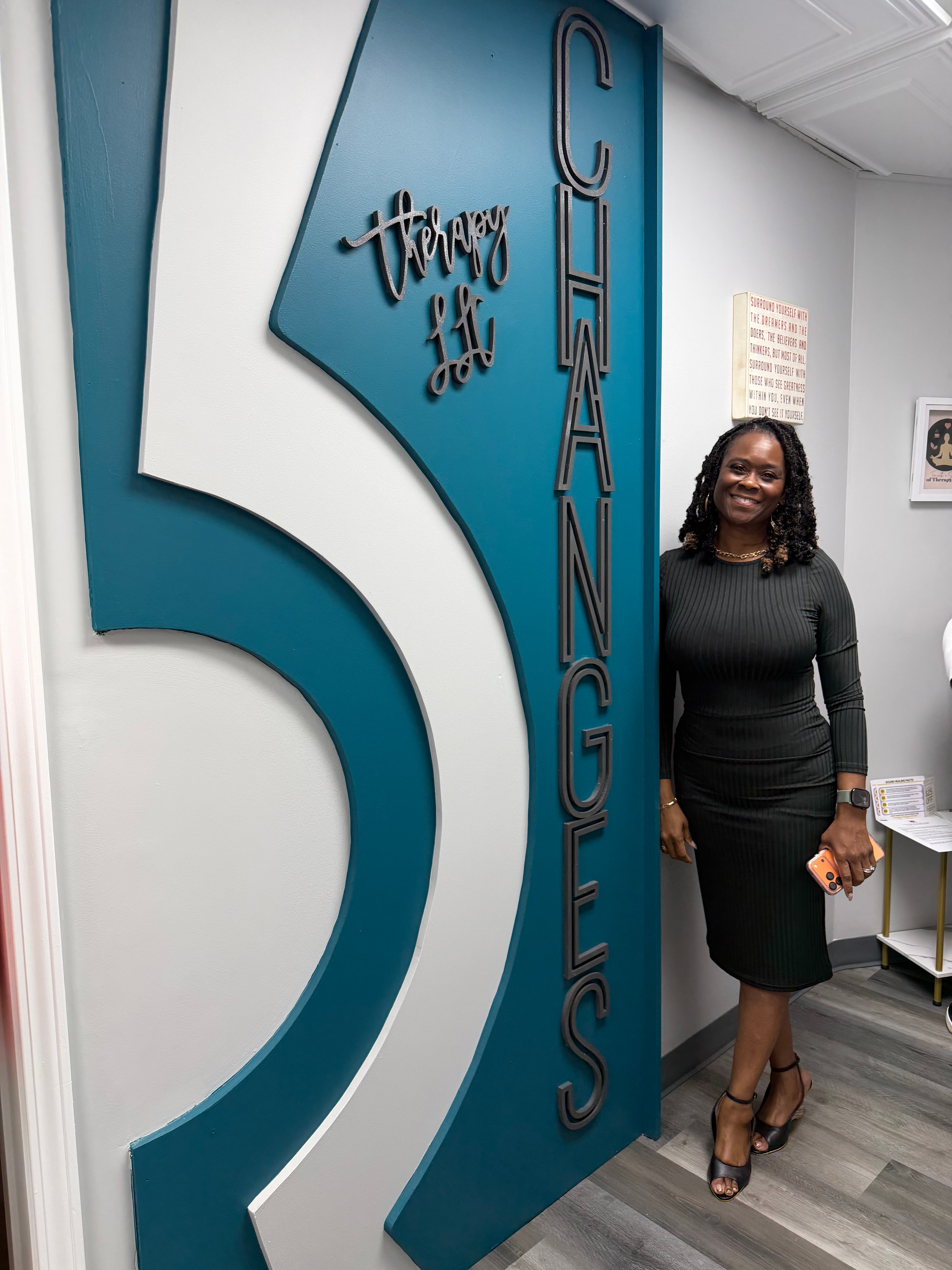 Changes Therapeutic Services team member standing beside the teal Changes wall sign