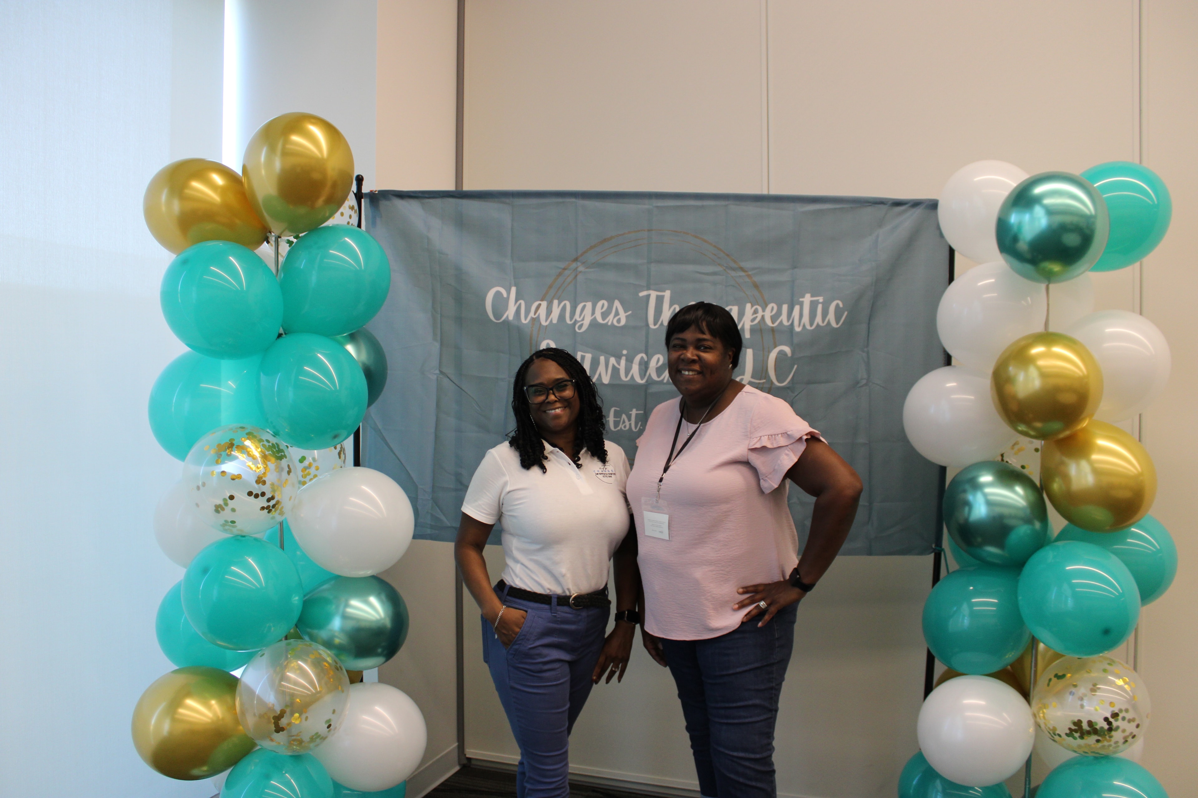 Two people posing in front of a Changes Therapeutic Services balloon backdrop
