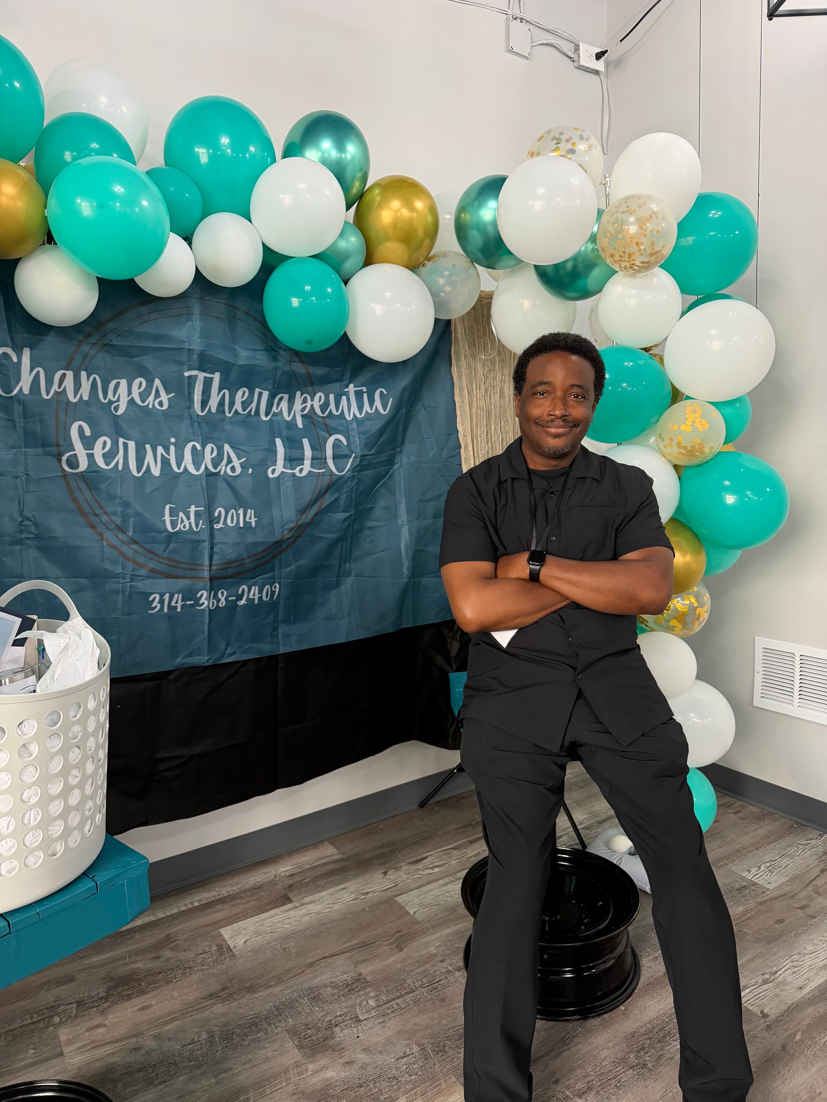 Changes Therapeutic Services team member posing beside a teal, white, and gold balloon display
