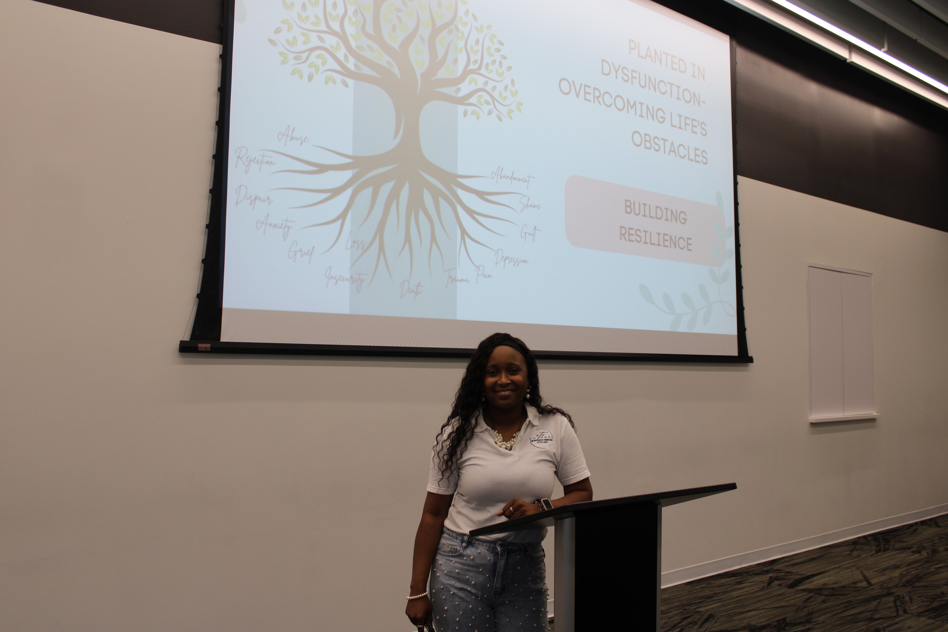 Presenter standing at a podium in front of a Building Resilience presentation