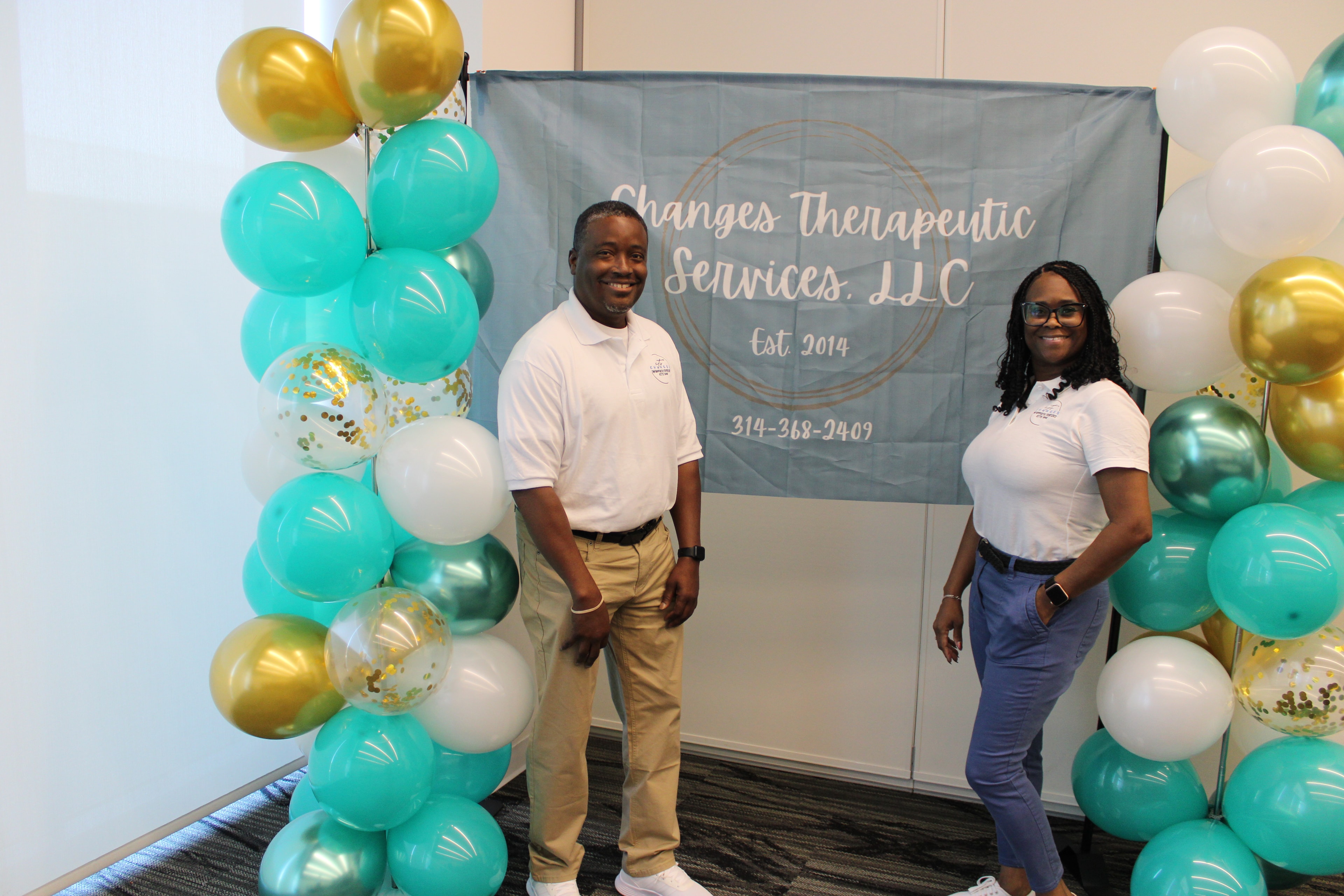 Two people posing beside the Changes Therapeutic Services celebration backdrop