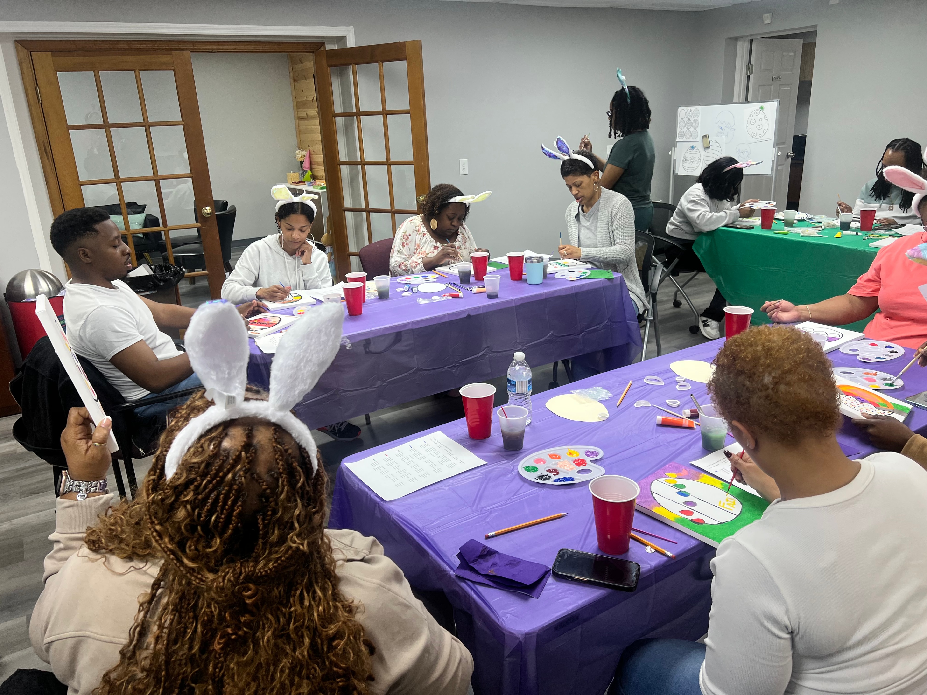 Participants wearing bunny ears and painting together at decorated tables during an Easter activity